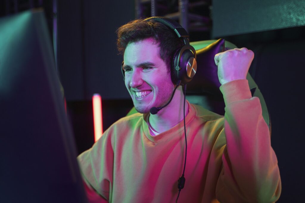 Gamer mit Headset auf dem Kopf, der auf einen Monitor schaut und sich freut.